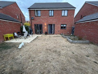 Standing at the back fence, looking straight back towards the house across the full length of the garden.