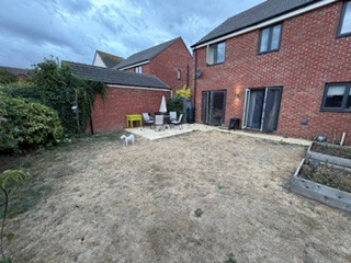 From the back left corner of the garden, looking back towards the house and the patio area.