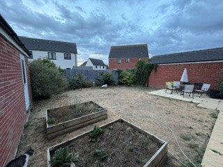 View from the garden gate looking across the space towards the neighbour's garage, with the raised beds and open ground visible.