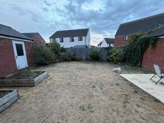Looking out from the house across the full garden, showing the open ground, raised beds, and boundaries.