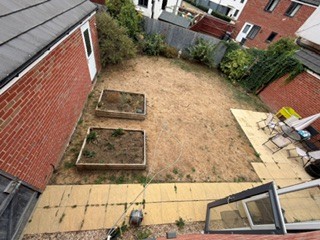 The garden seen from an upstairs window, showing the full rectangular space with two raised beds, bare earth, and the patio area.
